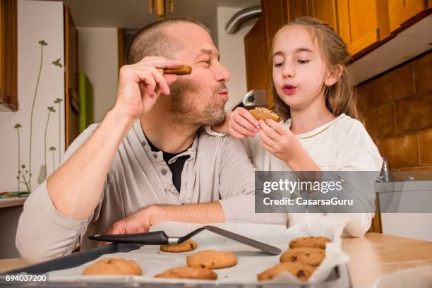 vater und elementare gealterten mädchen verkostung ein zuhause habe cookies zusammen - 2 männer essen kekse stock-fotos und bilder