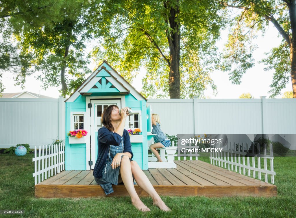 Frustrated woman drinking from can, children playing behind