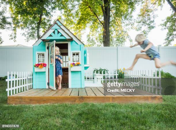 boy jumping fence, girl in play house looking concerned - playhouse stock-fotos und bilder