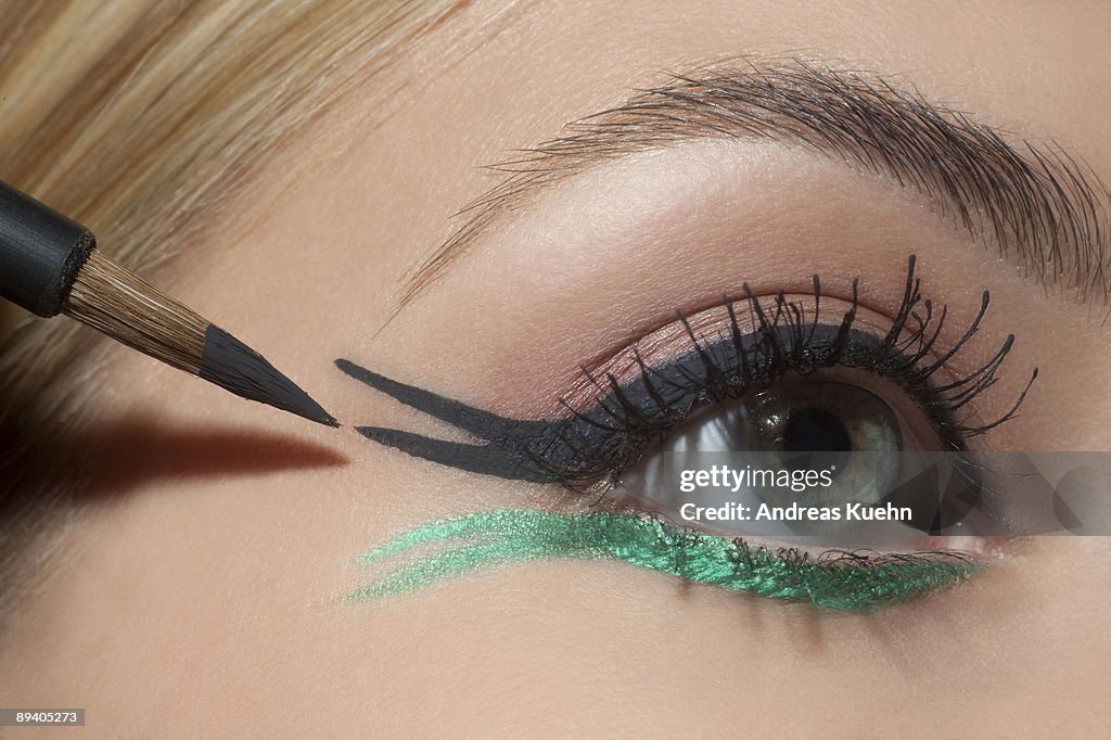 Young woman applying eye make up, close up.