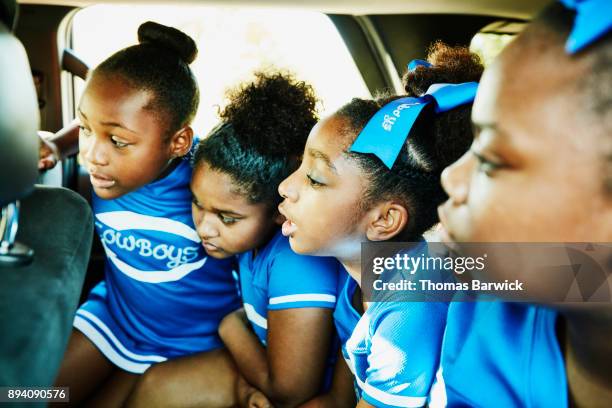 Young cheerleading teammates sitting in back seat of car on way to practice