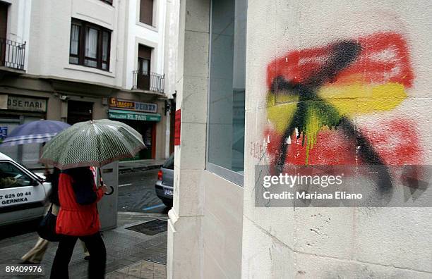 Two people walk through the streets under heavy rain. A graffiti shows a rejection to the Spanish flag in Gernika. Basque election set for April 17,...