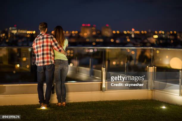 rear view of embraced couple looking at view from a penthouse terrace. - apartamento de cobertura imagens e fotografias de stock
