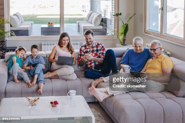 sonríe familia de múltiples generaciones utilizando la tecnología inalámbrica mientras se relaja en la sala de estar. - tablet smartphone fotografías e imágenes de stock