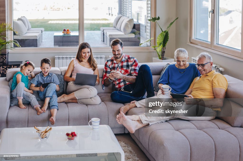 Família de várias gerações, usando a tecnologia sem fio enquanto relaxa na sala de estar a sorrir.