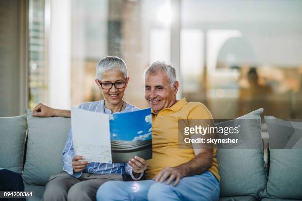 smiling mature couple relaxing on sofa at patio and reading magazine. - balcony reading stock pictures, royalty-free photos & images