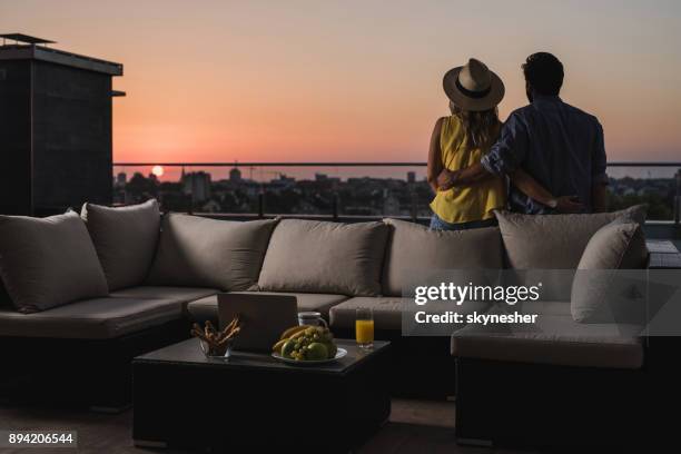 achteraanzicht van omarmd paar op zoek bij zonsopgang vanaf het terras van een penthouse. - penthouse stockfoto's en -beelden