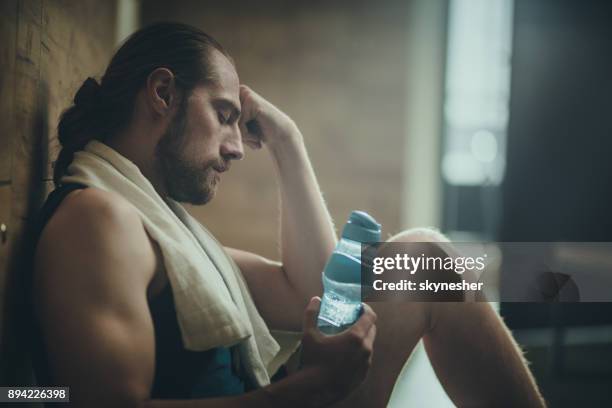 tired athletic man resting on water break at gym's dressing room. - man headache stock pictures, royalty-free photos & images