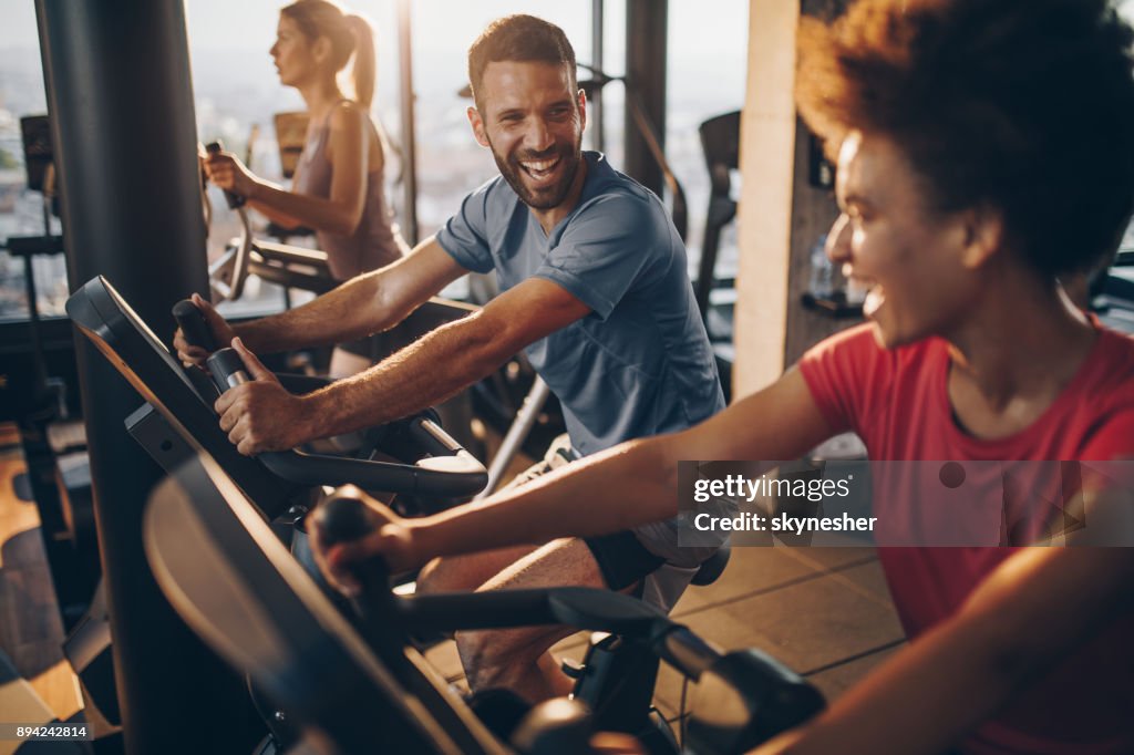 Fröhliche männlichen Athleten im Gespräch mit seinem Freund auf spinning Training in einem Fitnessstudio.