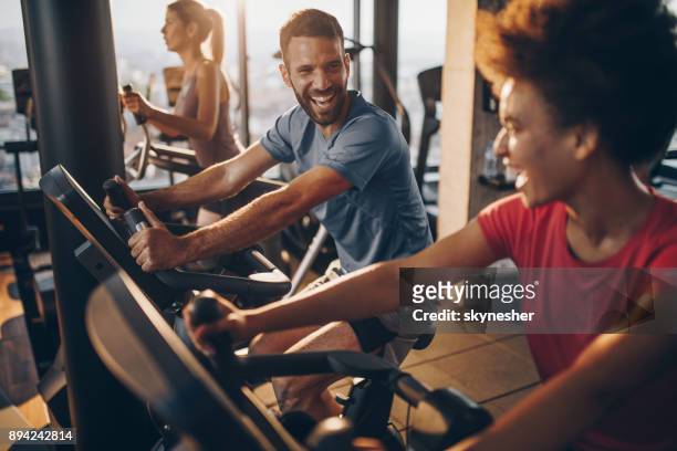 fröhliche männlichen athleten im gespräch mit seinem freund auf spinning training in einem fitnessstudio. - gym workout stock-fotos und bilder