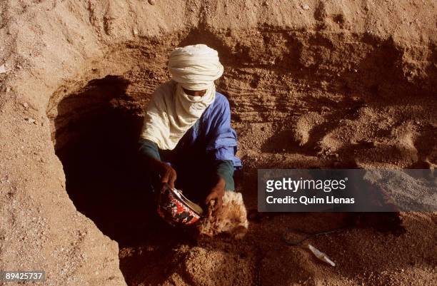 Travel to the Tuareg world of the Tassili, Algeria. Tuareg taking water from a hole in the dessert.