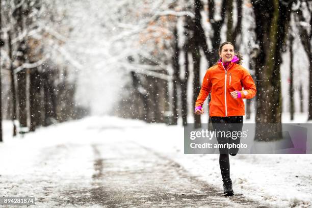 winter breaks - 40 years old woman running on country road through alley on cold winter day with snow and frost - jogging winter stock pictures, royalty-free photos & images