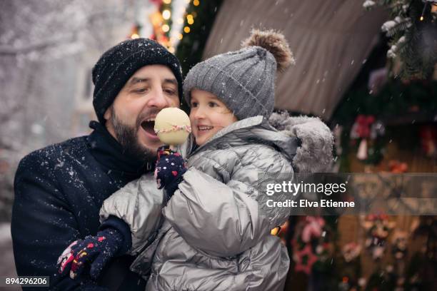father and child eating a white taffy apple, at a german christmas market in the snow - christmas treat stock pictures, royalty-free photos & images
