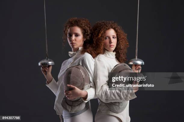 fencing sport competition. duel. dark grey background. sporting women. two curly redhead twin girls fencer. twins. - dueling stock pictures, royalty-free photos & images
