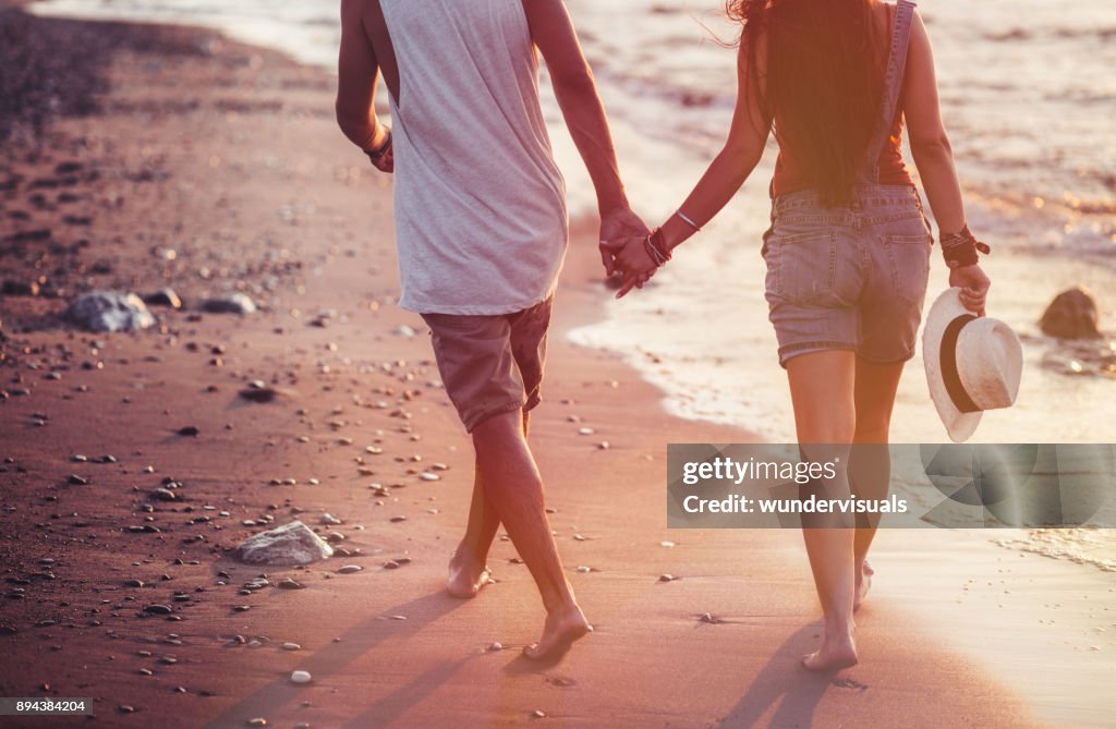 Young couple walking on beach and holding hands at sunset