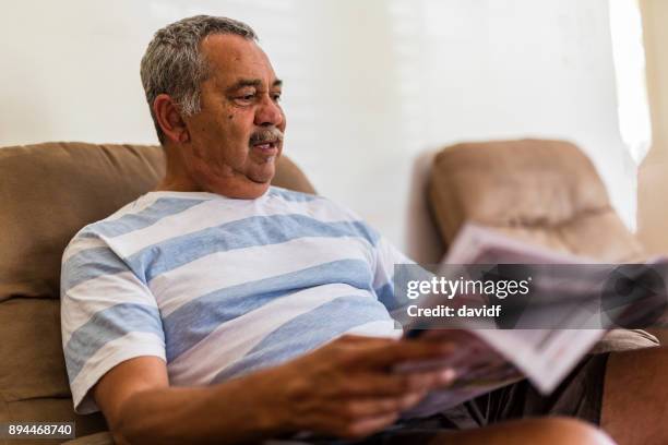 mature australian aboriginal man reading a newspaper at home - aboriginal man imagens e fotografias de stock