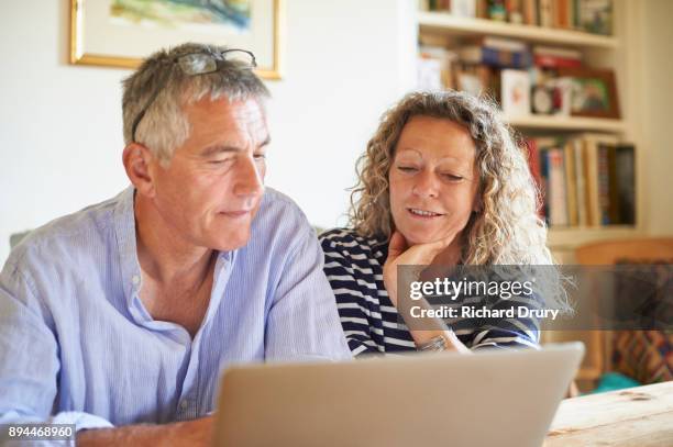 couple sitting at table using laptop - couple 50 55 laptop stock-fotos und bilder