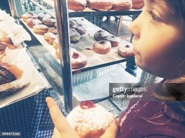 little girl tasting sufganiyot doughnuts in the bakery - sufganiyah photos et images de collection