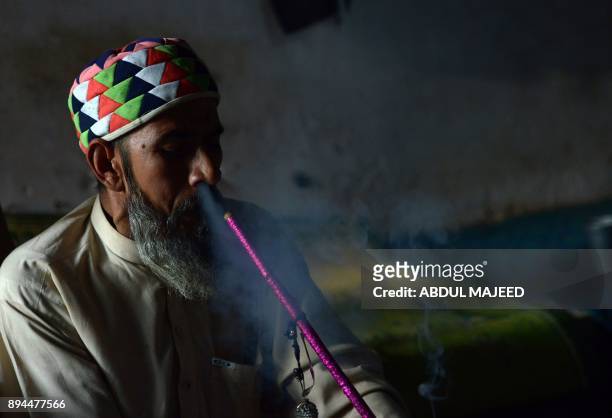 This picture taken on October 25, 2017 shows a Pakistani man smoking hashish in a chillum pipe near a shrine in Peshawar. In conservative Pakistan,...