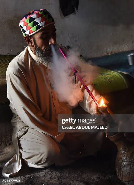 This picture taken on October 25, 2017 showing a Pakistani man smoking hashish in a chillum pipe near a shrine in Peshawar. In conservative Pakistan,...