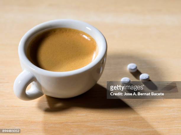 cup of coffee espresso in a cup of white porcelain with a few tablets of saccharin, on a table of wood illuminated by the light of the sun outdoors. spain. - capsule café stockfoto's en -beelden