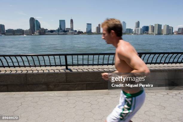 Young man jogging along the Hudson river near the Governor Nelson Rockefeller Park, on the background the skyline of the City of Jersey.