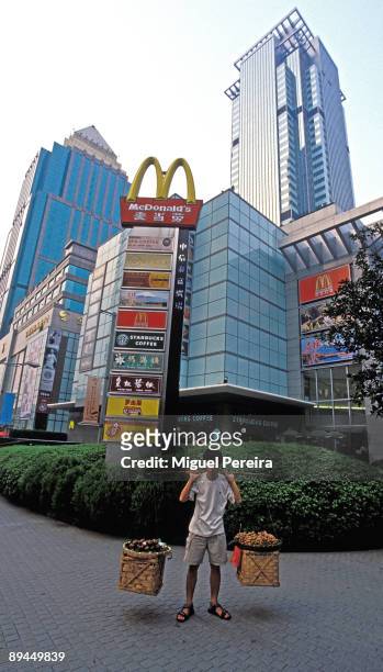 Young Chinese boy carries food baskets in front of a Shopping centre full of Occidental shops.