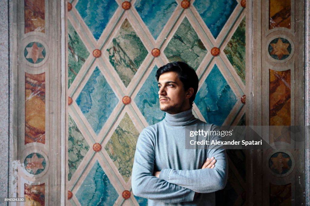 Portrait of a young man looking away arms crossed against the wall