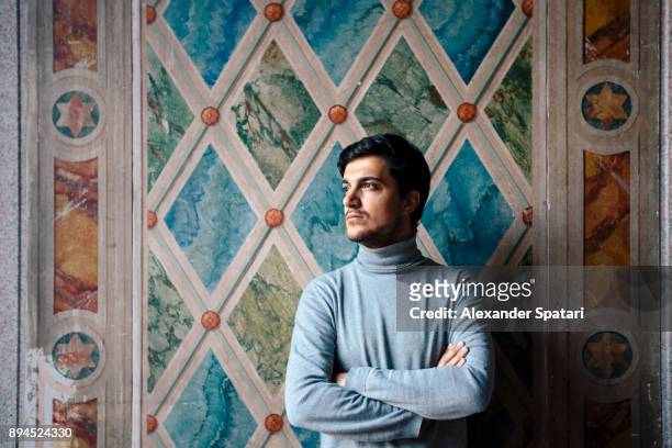 Portrait of a young man looking away arms crossed against the wall