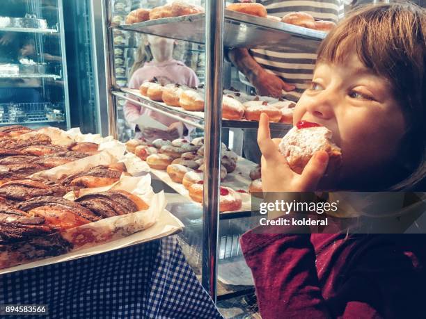 little girl tasting sufganiyot doughnuts in the bakery - sufganiyah photos et images de collection