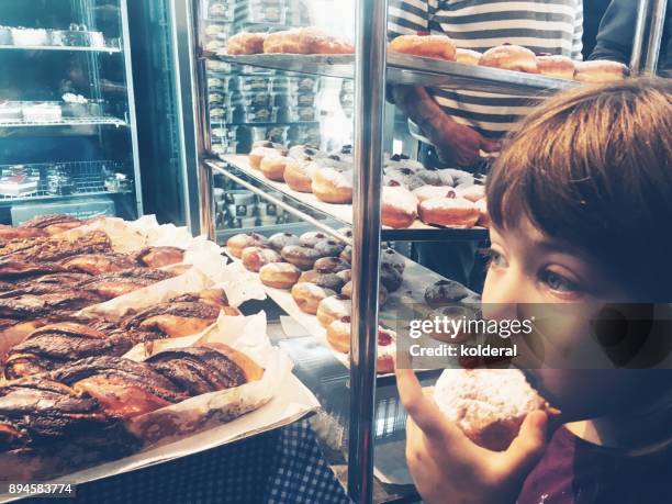 little girl tasting sufganiyot doughnuts in the bakery - sufganiyah stock-fotos und bilder