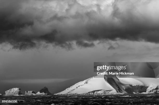 antarctica coastline with icebergs with dark cloud in sky. - marie hickman stock-fotos und bilder