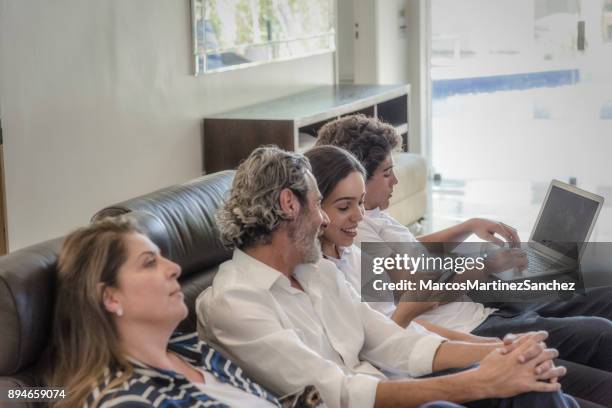 daughter showing on her cell phone, something curious, while the family is gathered in the living room - lypsesp17 stock pictures, royalty-free photos & images