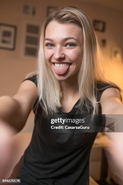beautiful cheerful teenage girl taking a selfie in domestic room - blonde girl sticking out her tongue stock pictures, royalty-free photos & images