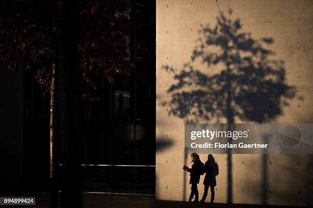 Woman reads a book next to a house facade and the shadow of a tree on December 18, 2017 in Berlin, Germany.