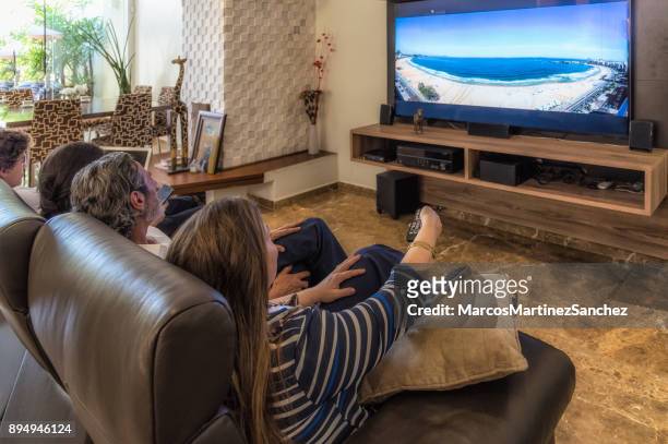 woman with remote control of the television with the family in the living room at leisure time - lypsesp17 stock pictures, royalty-free photos & images