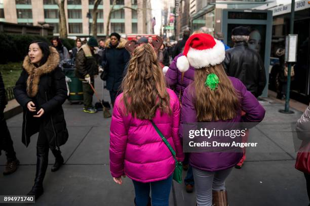 People wearing holiday attire walk along Fifth Avenue in Midtown Manhattan, December 18, 2017 in New York City. The city is decked out in holiday...