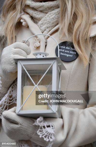 Worker of the Christmas market at Berlin's Charlottenburg Palace holds a candle and wears a button reading "...and terror will not defeat us!" to...