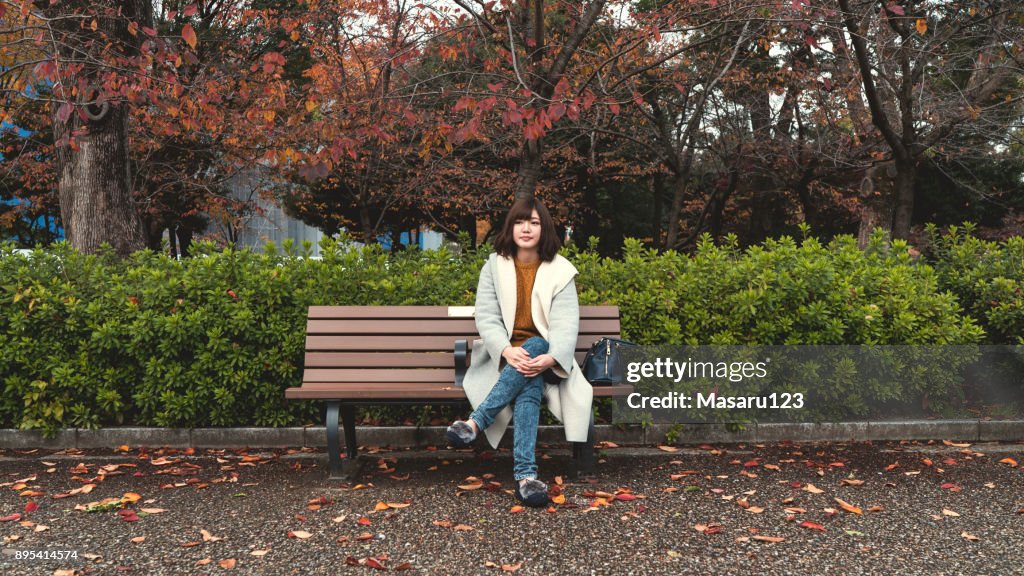 Vorderansicht einer jungen Frau sitzen auf einer Bank im Herbst