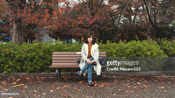 front view of a young woman sitting on a bench in autumn - banco de parque imagens e fotografias de stock