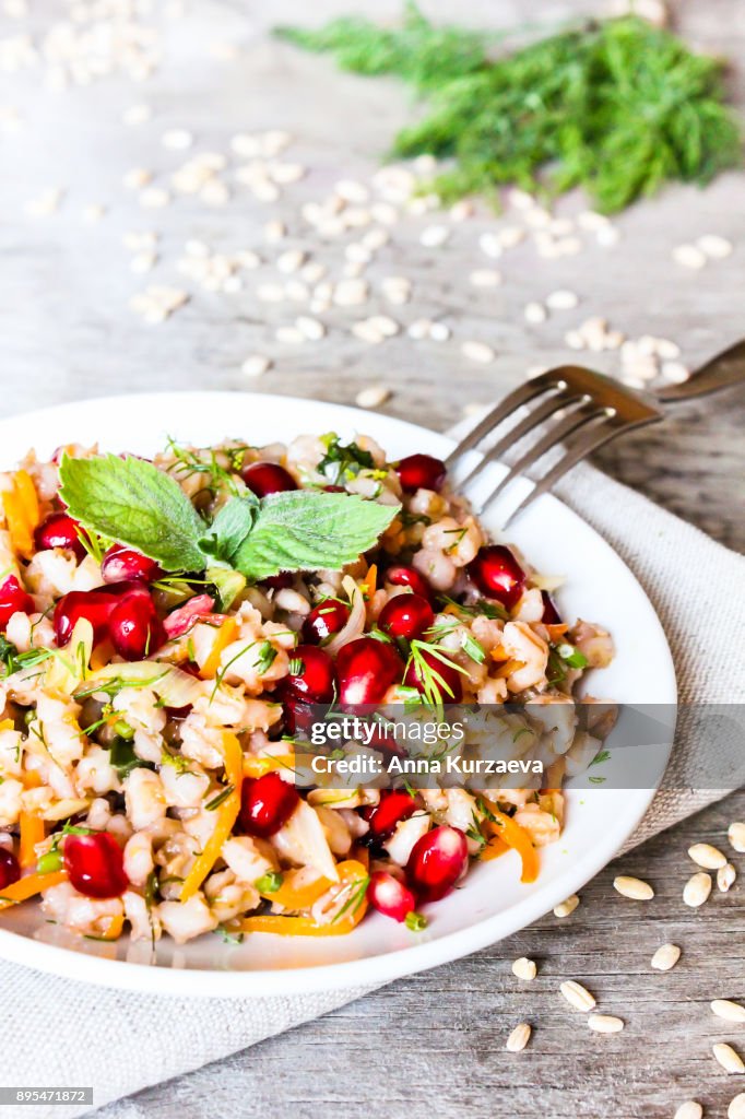 Warm salad with barley, carrot, onion, pomegranate seeds and fresh mint in a plate on a wooden table, selective focus