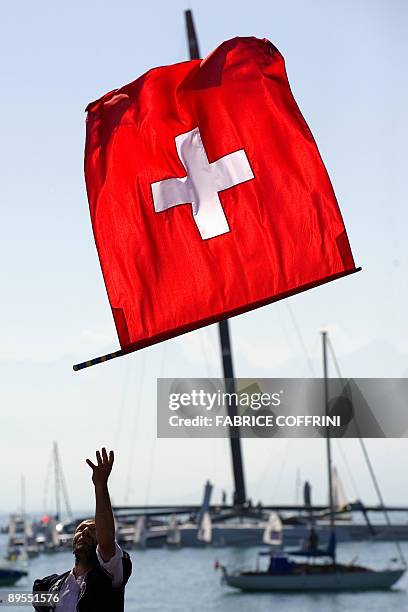 Man throws a Swiss flag with America's Cup defender Alinghi's new giant high tech catamaran "Alinghi 5" as background prior to its parade at Lake...