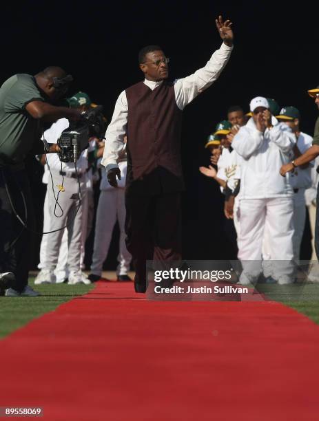 Hall of Fame baseball player Rickey Henderson waves to the crowd as he walks down a red carpet during a ceremony to retire his number 24 by the...