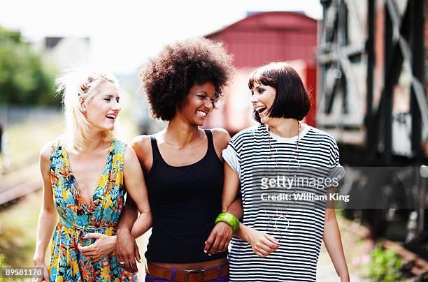 young adult females walking arm in arm - arm in arm stock pictures, royalty-free photos & images