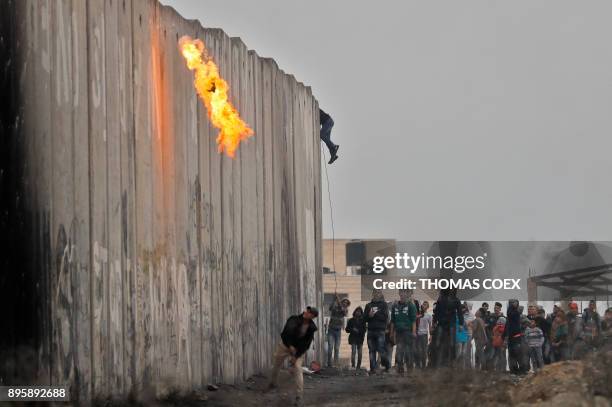 Palestinians throw a cocktail molotov and stones towards Israeli forces on the other side of a barrier at the Qalandia checkpoint in the occupied...