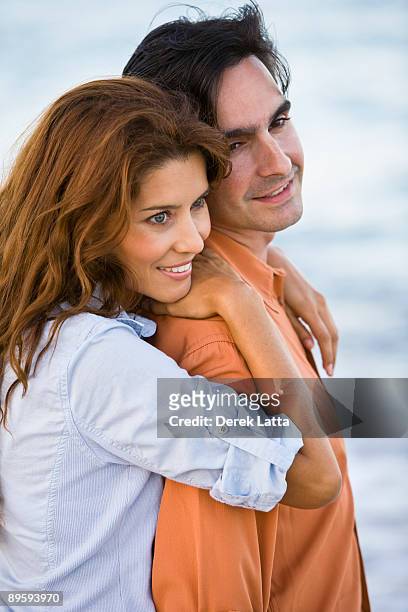 young hispanic couple embracing by ocean. - derek latta stock pictures, royalty-free photos & images