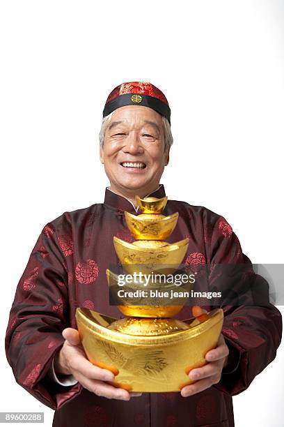 an elderly gentleman holds gold as a symbol of wealth and prosperity for chinese new year - abito tradizionale cinese foto e immagini stock
