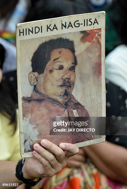 Manila resident holds up a poster showing the bloodied remains of Philippine opposition leader Benigno Aquino, with the words "You Are Not Alone"...