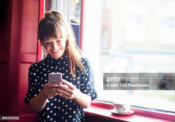 young woman using mobile phone near window - boa notícia imagens e fotografias de stock