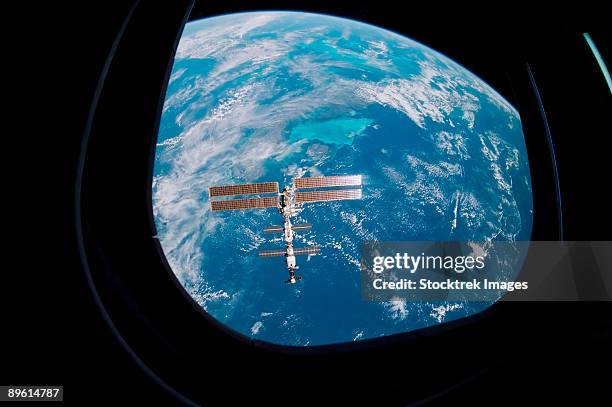 december 5-17, 2001 - backdropped against a blue and white earth, the international space station was photographed by one of the sts-108 crew members through an overhead window of the space shuttle endeavour. - iss window stock pictures, royalty-free photos & images